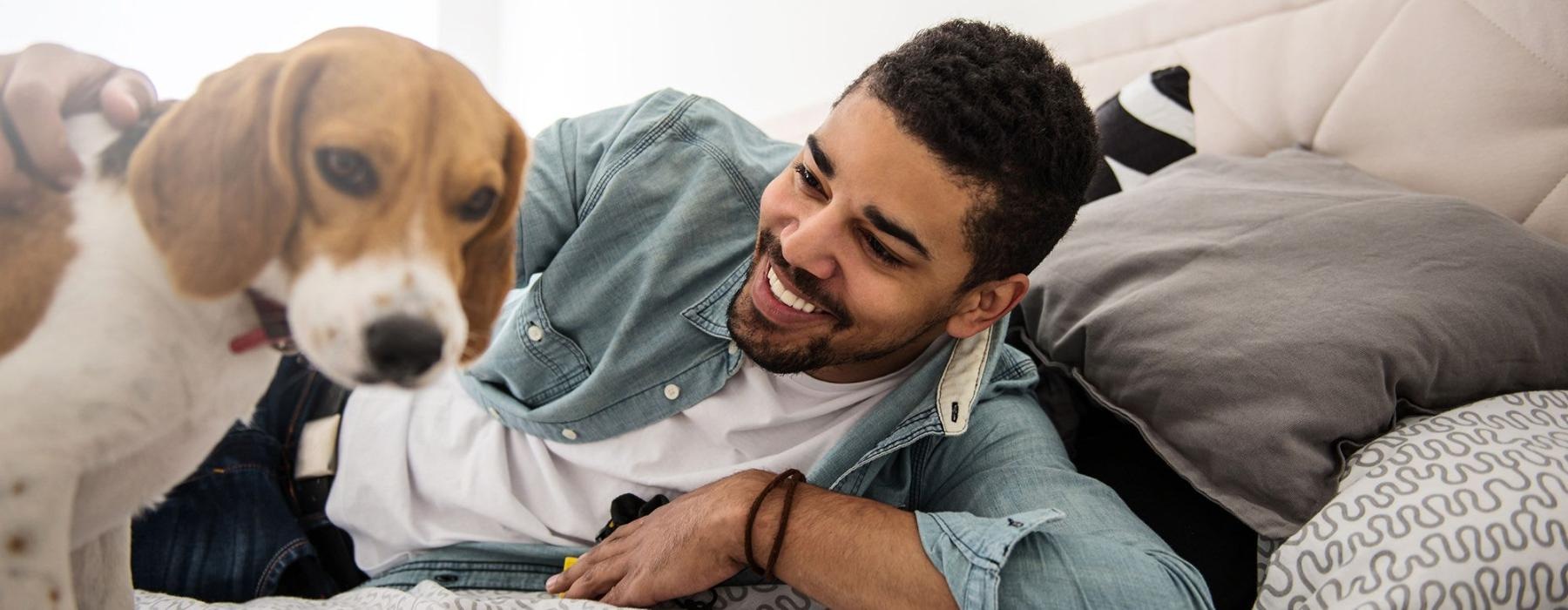 man smiles and pets his dog on a bed